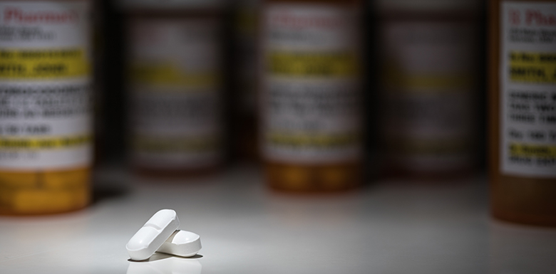 Two white pills on table with pill bottles blurred out in the background
