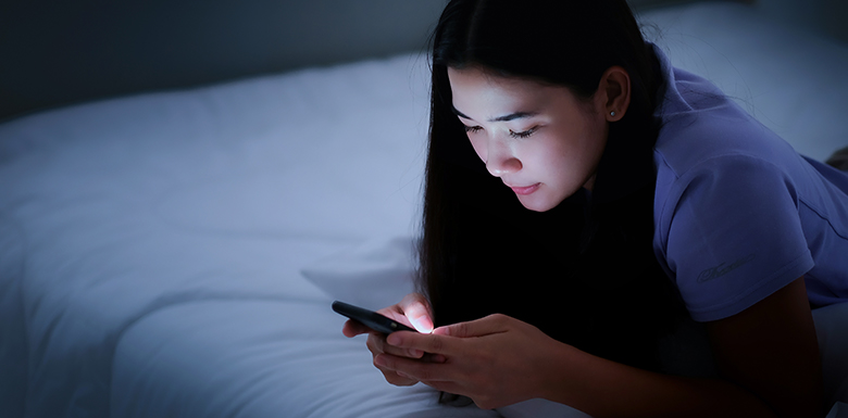 Young teen girl texting in her dark bedroom